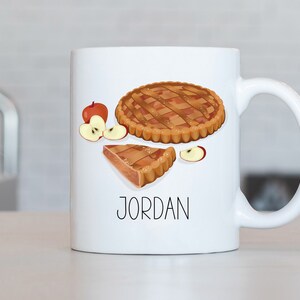 May include: White ceramic mug with a brown apple pie design and the name "JORDAN" printed on the front.