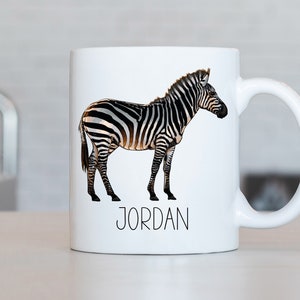 May include: White ceramic mug featuring a black and white zebra illustration with the name "JORDAN" printed in black beneath the zebra.