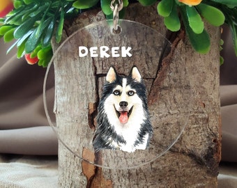 May include: A clear acrylic keychain with a woodgrain background featuring a black and white husky dog with blue eyes and a pink tongue. The text "DEREK" is printed in white on the keychain.