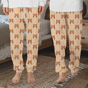 May include: A pair of tan pajama pants with a red panda face pattern. The pants have a drawstring waistband and a relaxed fit.