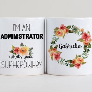 Puede incluir: Dos tazas de café blancas con texto negro y diseños florales. Una taza dice "Soy un administrador, ¿cuál es tu superpoder?" y la otra taza tiene una corona de flores con el nombre "Gabriella" en el centro.