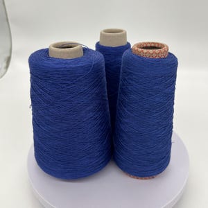 May include: Three spools of vibrant blue thread are displayed on a white surface. The thread is tightly wound around cardboard cores. The spools vary slightly in size, creating a visually interesting arrangement. The color is a deep, saturated blue.