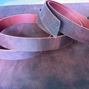 Puede incluir: Primer plano de varias tiras de cuero azul grisáceo con un interior marrón rosado. Las tiras de cuero están enrolladas y dispuestas sobre una superficie texturizada, mostrando las variaciones de color y la textura del material. La imagen resalta los tonos naturales del cuero.