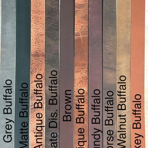 May include: A vertical display of leather strips in various colors, including grey, black, brown, and burgundy. Each strip is labeled with a color name, such as "Grey Buffalo" and "Whiskey Buffalo". The textures vary from matte to distressed.