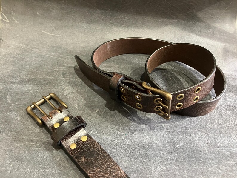 May include: Two brown leather belts with brass buckles and eyelets. One belt has a double row of eyelets and the other has a single row.
