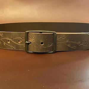 May include: A brown leather belt with a floral design and a silver buckle.