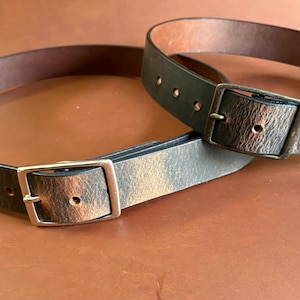 Pode incluir: Dois cintos de couro com fivelas prateadas. Os cintos são marrons e pretos com um visual envelhecido.