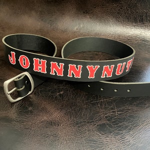 May include: Black leather belt with the name "JOHNNY NUT" in red lettering.