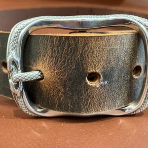 Op de afbeelding: Een bruine leren riem met een zilveren slangvormige gesp. De gesp heeft een gedetailleerd ontwerp en een gepolijste afwerking.