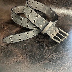 May include: A gray leather belt with silver grommets and a silver buckle. The belt is rolled up and the buckle is visible.