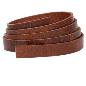 May include: A roll of brown leather strips. The leather has a textured surface and a warm, reddish-brown colour. The strips are coiled, revealing the edges and the grain of the material. The leather appears to be of high quality.