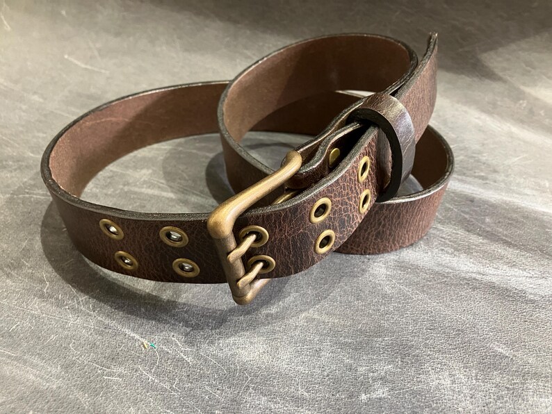 May include: A brown leather belt with a brass buckle and multiple eyelets. The belt is worn and has a distressed look.