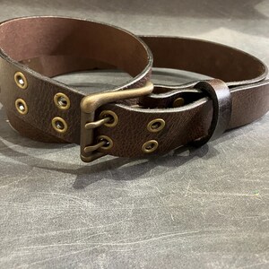 May include: A brown leather belt with a brass buckle and double rows of eyelets.