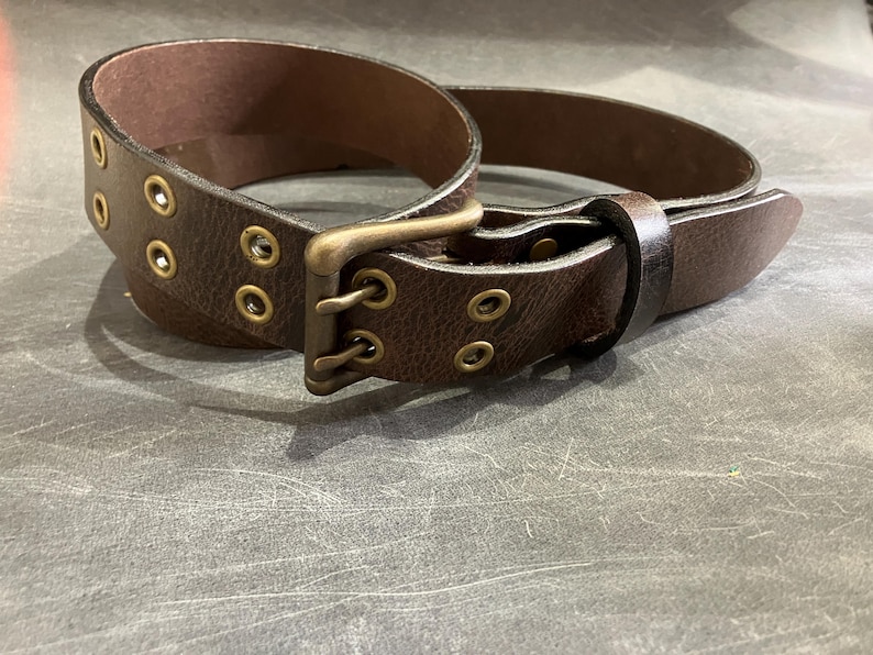 May include: A brown leather belt with a brass buckle and double rows of eyelets.