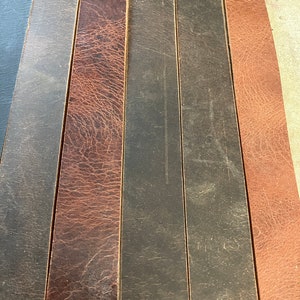May include: Close-up of eight leather strips in various shades of brown and black. The strips are arranged side-by-side, showcasing the different textures and colors of the leather.