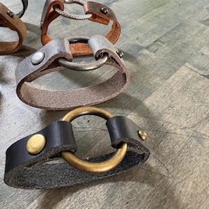May include: Four leather bracelets with different metal clasps. The bracelets are in various shades of brown and gray. The clasps are silver, brass, and a combination of both.