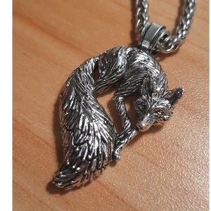 Puede incluir: Un collar con un colgante de plata en forma de zorro, con un dise&ntilde;o detallado de una cola de zorro enroscada y una cabeza de zorro. El collar est&aacute; en una cadena de plata.