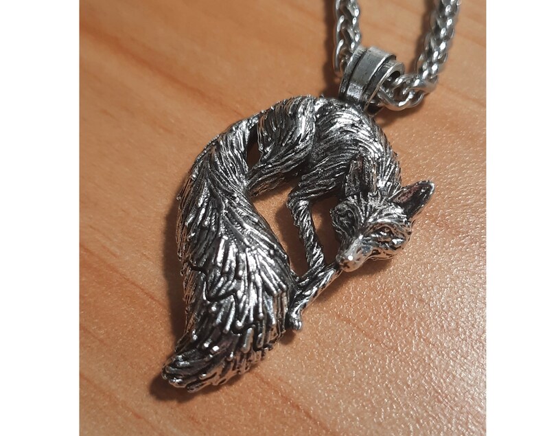 Puede incluir: Un collar con un colgante de plata en forma de zorro, con un dise&ntilde;o detallado de una cola de zorro enroscada y una cabeza de zorro. El collar est&aacute; en una cadena de plata.