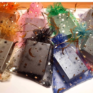 Puede incluir: Surtido de peque&ntilde;as cajas de regalo envueltas en tela transparente de colores con un patr&oacute;n de estrellas. Las cajas son grises y tienen un dise&ntilde;o de media luna.