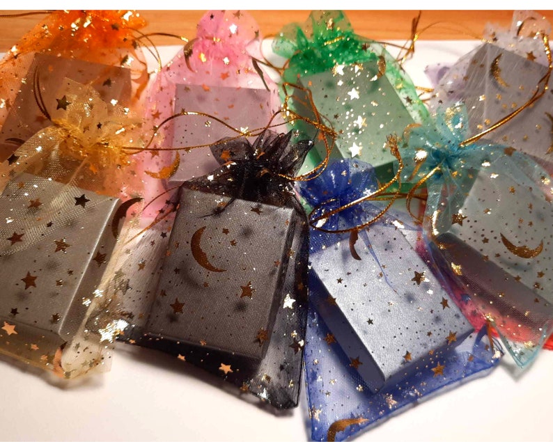 Puede incluir: Surtido de peque&ntilde;as cajas de regalo envueltas en tela transparente de colores con un patr&oacute;n de estrellas. Las cajas son grises y tienen un dise&ntilde;o de media luna.