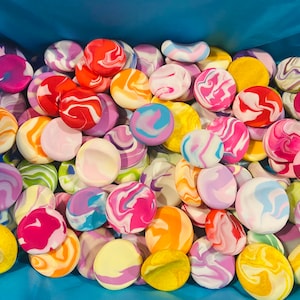May include: A collection of colourful, swirled, round, decorative stones in a blue box. The stones are made of clay and have a variety of colours, including pink, blue, yellow, green, and orange.