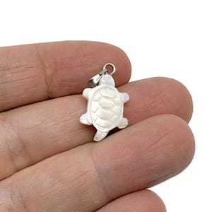 Könnte beinhalten: Ein weißer Perlmutt-Schildkröten-Anhänger mit einer silbernen Öse.