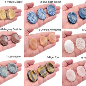 Peut inclure: Neuf types de pierres polies de forme ovale, chacune avec une couleur et un motif uniques. Les pierres sont dispos&eacute;es en trois rang&eacute;es de trois, chaque pierre &eacute;tant tenue dans une main. Les pierres sont &eacute;tiquet&eacute;es avec leurs noms, tels que "Picture Jasper", "Blue Spot Jasper" et "Sodalite".