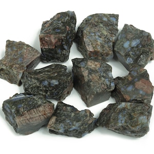 Könnte beinhalten: Eine Ansammlung von rohen Steinen mit einer Mischung aus dunkelblauen, braunen und grauen Farbtönen. Die Steine haben eine strukturierte Oberfläche und unregelmäßige Formen, was darauf hindeutet, dass es sich um natürliche Exemplare handelt. Die Anordnung ist vor einem weißen Hintergrund verstreut.