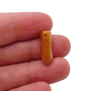 Könnte beinhalten: Ein kleiner, spitzer, orangebrauner Edelstein-Anhänger mit einem Loch oben zum Aufziehen.