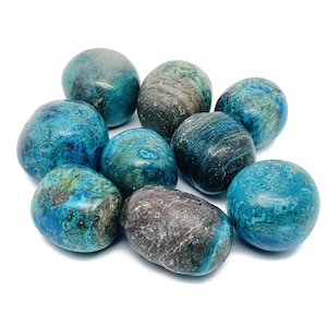 Peut inclure: Un ensemble de pierres polies, de forme ovale, dans des tons de bleu sarcelle, bleu et gris. Les pierres présentent une texture lisse et brillante avec des motifs variés. L'arrangement est sur fond blanc, mettant en valeur les couleurs et textures naturelles.