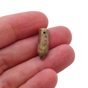 May include: A small, pointed, green, pink and brown stone pendant with a hole drilled through the top for hanging.