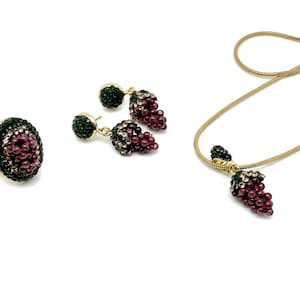 May include: A gold necklace, ring, and earrings set with a grape design. The grapes are made of purple and green crystals.