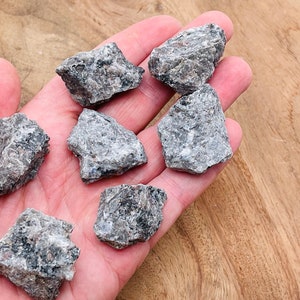 May include: A collection of six small, rough, gray and black stones. The stones are in a hand, and the background is a light brown wooden surface.
