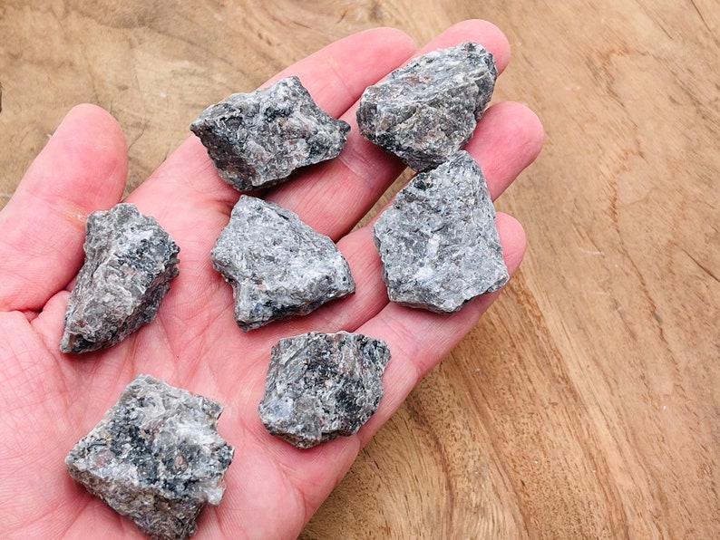 May include: A collection of six small, rough, gray and black stones. The stones are in a hand, and the background is a light brown wooden surface.