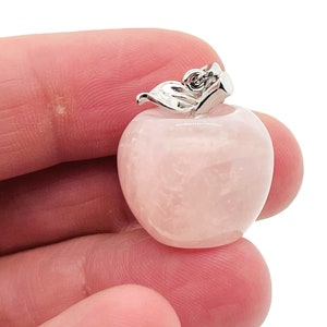 Op de afbeelding: Een roze rozenkwarts appel hanger met een zilveren blad ontwerp. De hanger wordt in een hand gehouden.