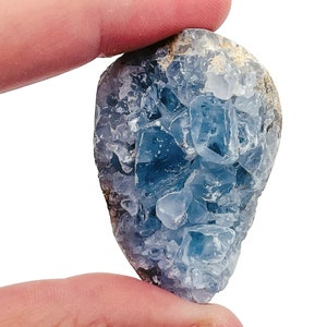 May include: A blue celestite crystal with a rough, natural texture. The crystal has a cluster of smaller crystals on the surface.