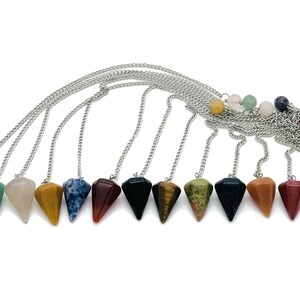 May include: A collection of gemstone pendulums with silver chains. The pendulums are various colors, including clear, green, yellow, blue, red, black, and brown. The gemstones are faceted and cone-shaped, and the chains are attached at the top.