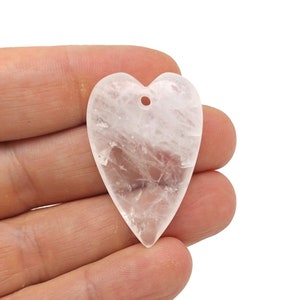 Puede incluir: Un colgante de corazón de cuarzo transparente con un agujero para encordar. El corazón es liso y pulido, con una apariencia ligeramente nublada.