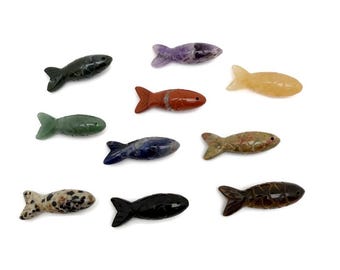 May include: A collection of ten carved stone fish figurines in various colors, including green, black, and purple. The fish are arranged on a white surface, showcasing their detailed craftsmanship and unique textures.
