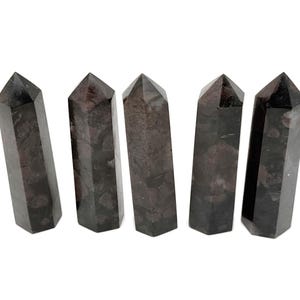May include: Five black and grey crystal points, also known as wands, are arranged in a row. The points are all roughly the same size and shape, and they have a smooth, polished finish.