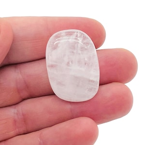 May include: A smooth, white, oval-shaped crystal stone. The stone is translucent and has a slightly cloudy appearance.