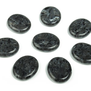 May include: Eight smooth, oval-shaped black stones with a speckled pattern. The stones are arranged in a circle on a white background.