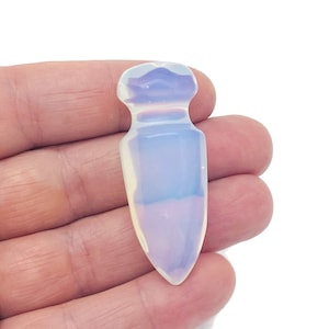 Puede incluir: Una punta de cristal de ópalo blanco con una punta puntiaguda y una parte superior redondeada. El cristal es translúcido y tiene un color blanco lechoso.