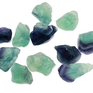 May include: A collection of ten green and purple fluorite crystals. The crystals are rough and have a natural, unpolished look.