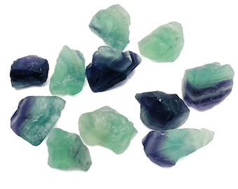 May include: A collection of ten green and purple fluorite crystals. The crystals are rough and have a natural, unpolished look.