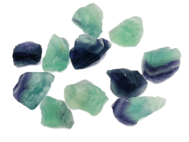 May include: A collection of ten green and purple fluorite crystals. The crystals are rough and have a natural, unpolished look.