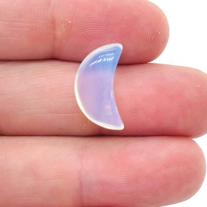 Puede incluir: Una pieza de ópalo en forma de media luna, de color blanco lechoso y azul claro.