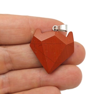 May include: Red gemstone pendant in a geometric diamond shape with a silver bail. The pendant is faceted and has a reddish-brown color.