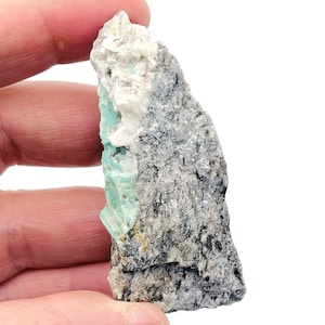 May include: A rough, gray rock with a green emerald crystal embedded in it.