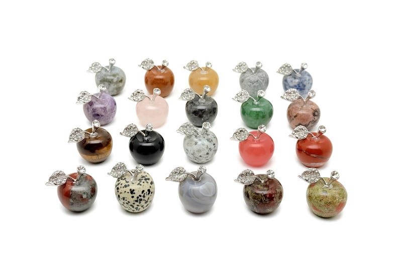 May include: A collection of 20 gemstone apple figurines. Each apple is carved from a different type of gemstone, including amethyst, rose quartz, tiger's eye, and jasper. The apples are all about 2 inches tall and have a silver-toned metal stem and leaves.